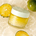 A jar of Goodal Vita-C Dark Spot Care Cream surrounded by fresh green tangerines, its main ingredient, floating against a light, watery background.