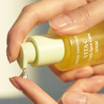 A hand holding the Goodal Green Tangerine Vita-C Dark Spot Care Serum bottle, dispensing a drop onto a fingertip in soft, natural lighting.