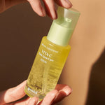 A hand holding a glass bottle of Goodal Green Tangerine Vita-C Dark Spot Care Serum, highlighting its vibrant yellow liquid.