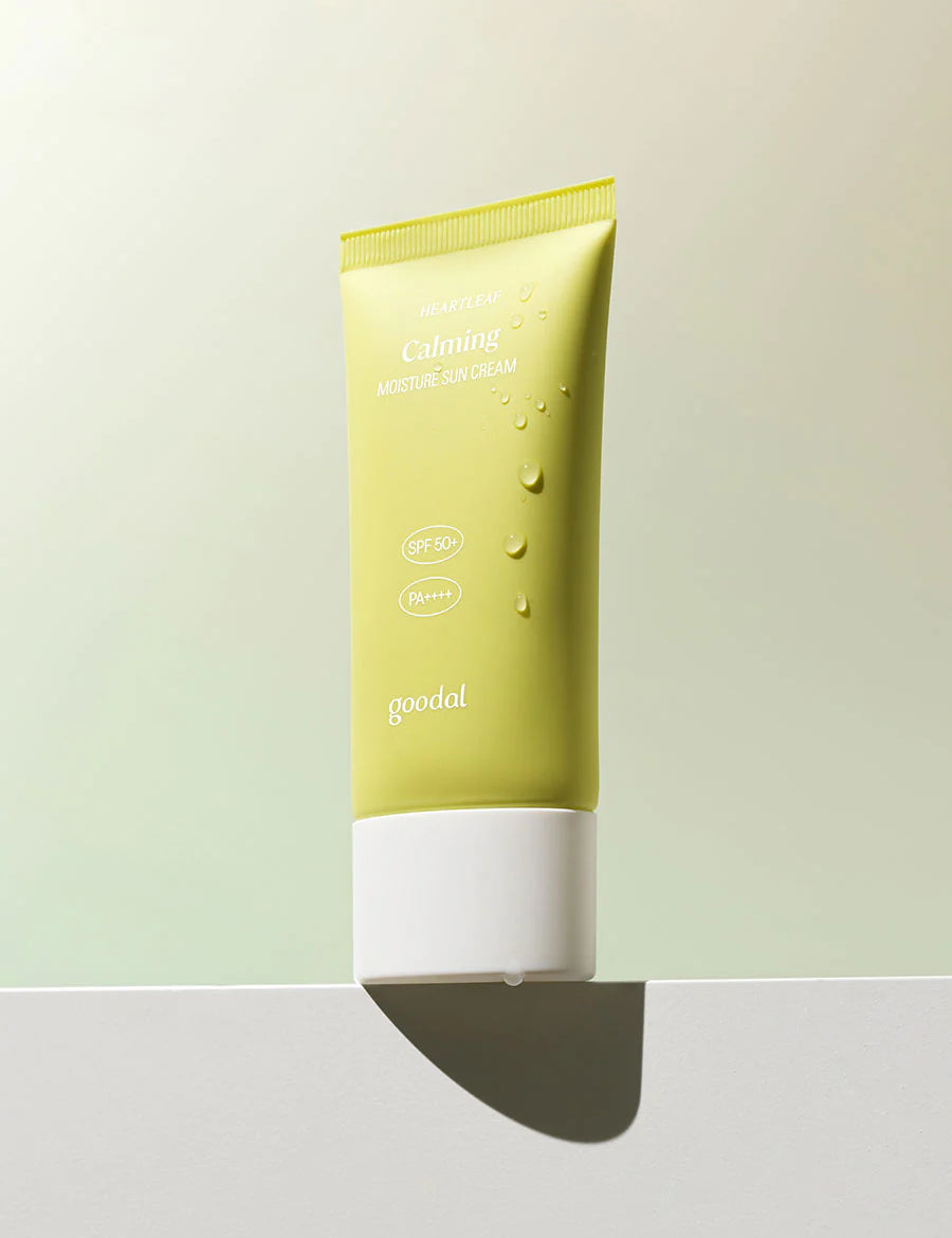 A pastel green tube of Goodal Houttuynia Cordata Calming Moisture Sun Cream with SPF 50+ and PA++++, resting on a white ledge with water droplets.