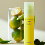 A bright yellow bottle of Goodal Green Tangerine Vita C Dark Circle Eye Cream, set on a soft, light surface with green tangerines in the background, highlighting its main ingredient.