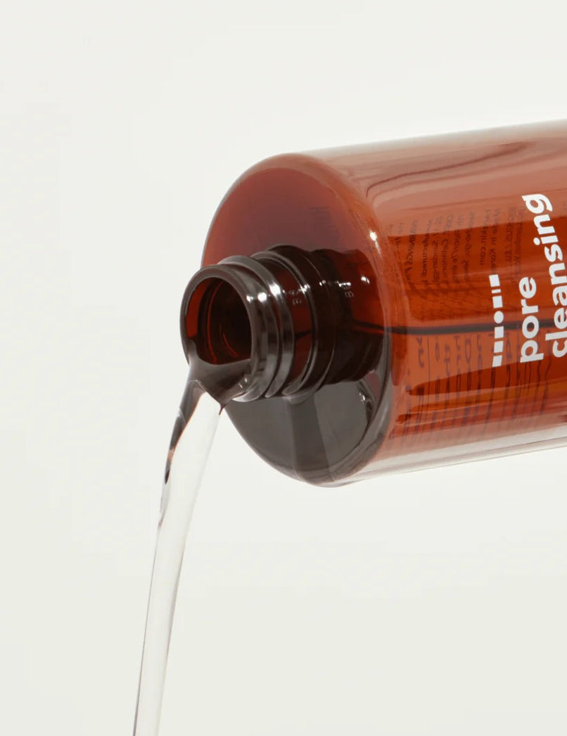 Hanskin Pore Cleansing Oil dispensing clear liquid against a neutral background, highlighting its lightweight texture.