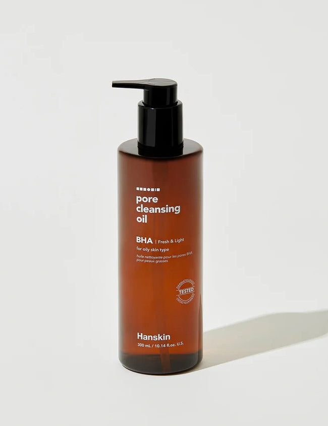 A brown bottle of Hanskin Pore Cleansing Oil with a pump dispenser, labeled for oily skin and formulated with BHA, featuring a 300 mL capacity.