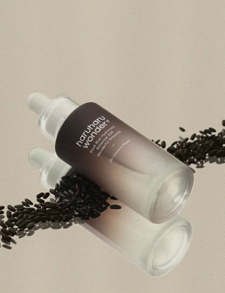 Haruharu Wonder Black Rice Hyaluronic Botanical 2GF Wonderful Ampoule surrounded by black rice grains on a soft beige background.