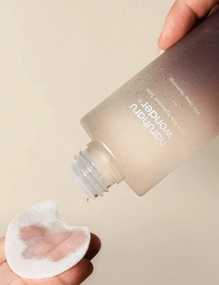 A hand holding Haruharu Wonder Black Rice Hyaluronic Toner, pouring onto a cotton pad, highlighting its lightweight texture.