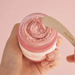 A hand holding a jar of 'I'm From Beet Purifying Mask' pink cream with a wooden spatula hovering above, set against a soft pink background, highlighting its creamy, antioxidant-rich formula.
