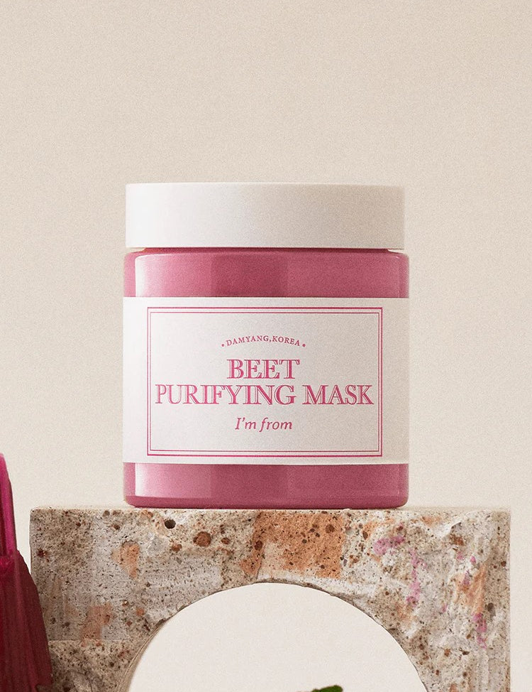 A pink jar of 'I'm From Beet Purifying Mask' displayed on a textured stone pedestal against a soft, neutral background, emphasizing its antioxidant and skin-purifying benefits.