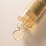 A bottle of 'I'm From' Mugwort Essence tipped over, with a droplet of golden liquid pooling on a light surface.