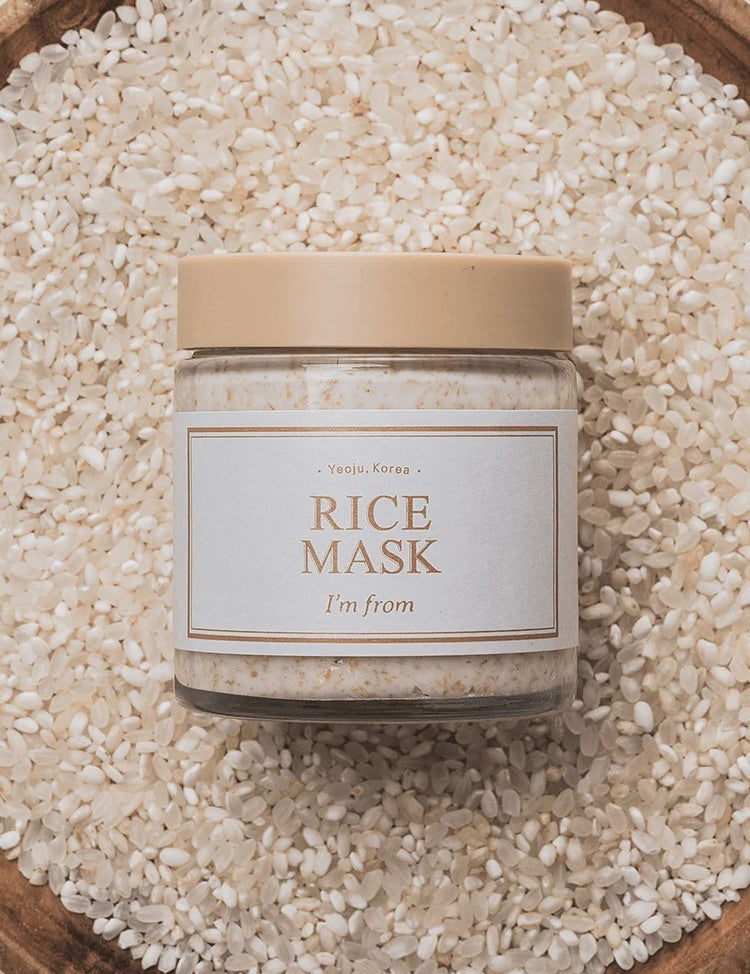 A jar of 'I'm From' Rice Mask placed on a bed of white rice in a wooden bowl, highlighting its main ingredient.
