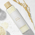 A bottle of 'I'm From' Rice Toner on a white background, surrounded by rice grains and a rice stalk.