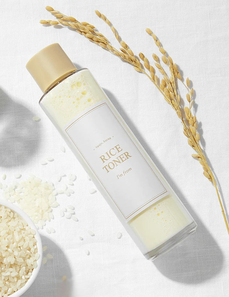 A bottle of 'I'm From' Rice Toner on a white background, surrounded by rice grains and a rice stalk.