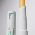 Innisfree Canola Honey Lip Balm with a visible yellow stick, housed in a white container with green lettering, set against a light background.