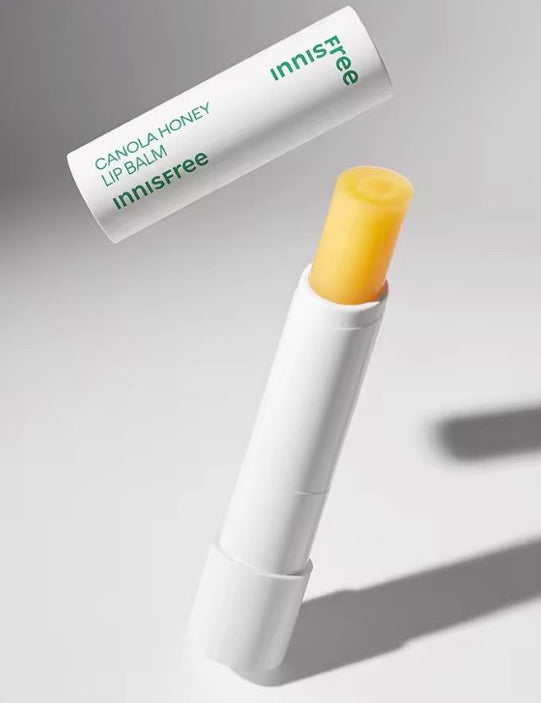Innisfree Canola Honey Lip Balm with a yellow tip, partially out of the white tube, showcasing its smooth texture and bright yellow color.