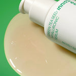 Close-up of Innisfree Green Tea Seed Hyaluronic Serum bottle with its glossy texture drop on a vibrant green background, highlighting its hydrating formula.