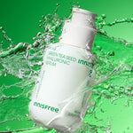 White bottle of Innisfree Green Tea Seed Hyaluronic Serum surrounded by splashes of water against a vibrant green background, emphasizing hydration and freshness.