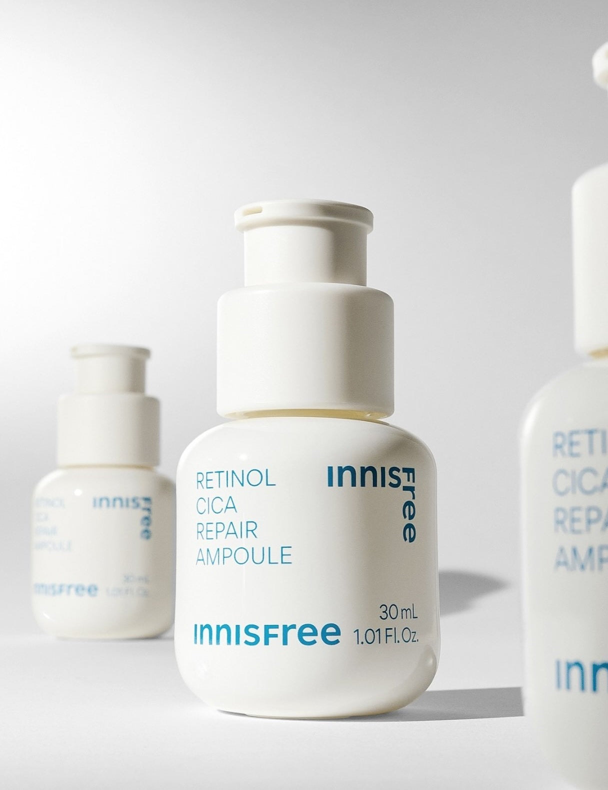 Three white bottles of Innisfree's Retinol Cica Repair Ampoule, each labeled with blue text, on a minimalist backdrop.