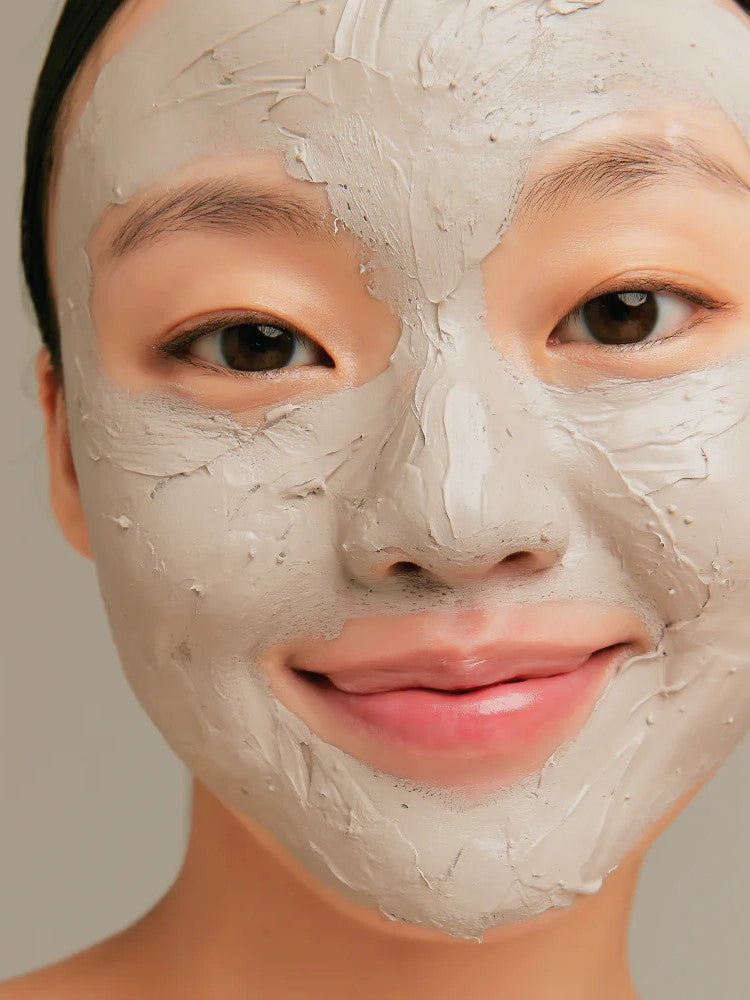 A model applies the Innisfree Super Volcanic Pore Clay Mask to her face, showcasing its gray clay texture.