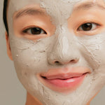 A model applies the Innisfree Super Volcanic Pore Clay Mask to her face, showcasing its gray clay texture.