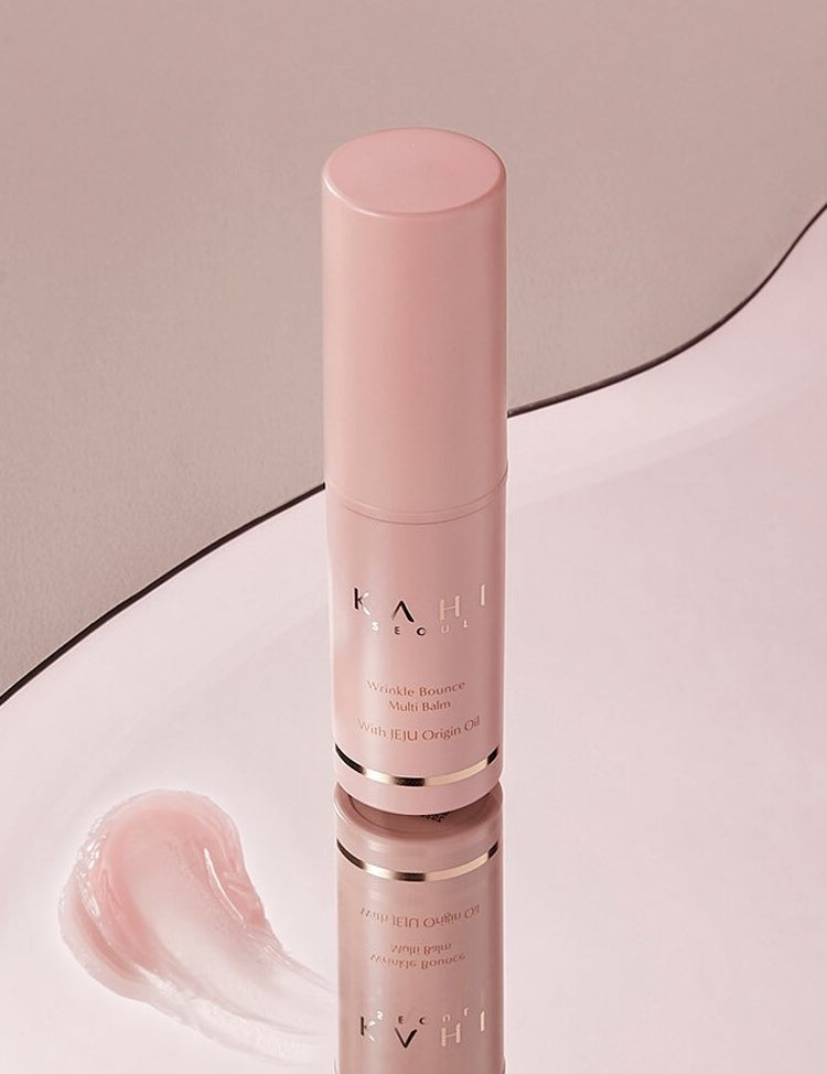 A pink Kahi Wrinkle Bounce Multi Balm bottle reflecting on a smooth surface, accompanied by a creamy swatch of the balm.
