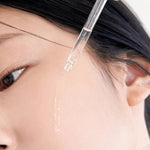 Close-up of a dropper dispensing Klairs Freshly Juiced Vitamin Drop onto a model's cheek, highlighting the serum's lightweight texture and brightening benefits.