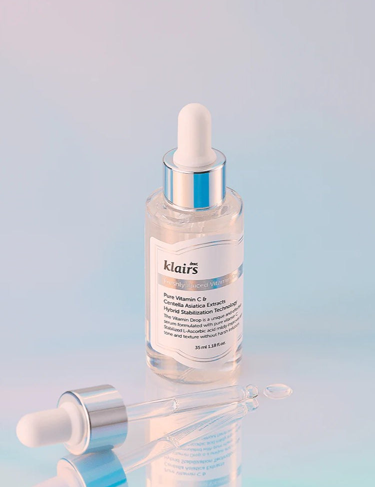 Klairs Freshly Juiced Vitamin Drop in a transparent serum bottle with a dropper, set against a soft pastel gradient background, emphasizing its brightening formula.