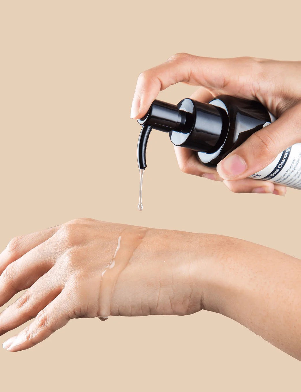 Hand applying a pump of Klairs Gentle Black Deep Cleansing Oil to another hand, showcasing its smooth texture against a beige background.