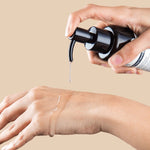 Hand applying a pump of Klairs Gentle Black Deep Cleansing Oil to another hand, showcasing its smooth texture against a beige background.