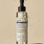 Klairs Gentle Black Fresh Cleansing Oil in a sleek bottle with a pump, surrounded by glistening water droplets on a textured surface.