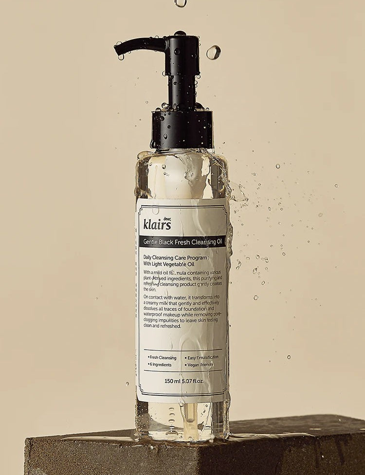 Klairs Gentle Black Fresh Cleansing Oil in a sleek bottle with a pump, surrounded by glistening water droplets on a textured surface.