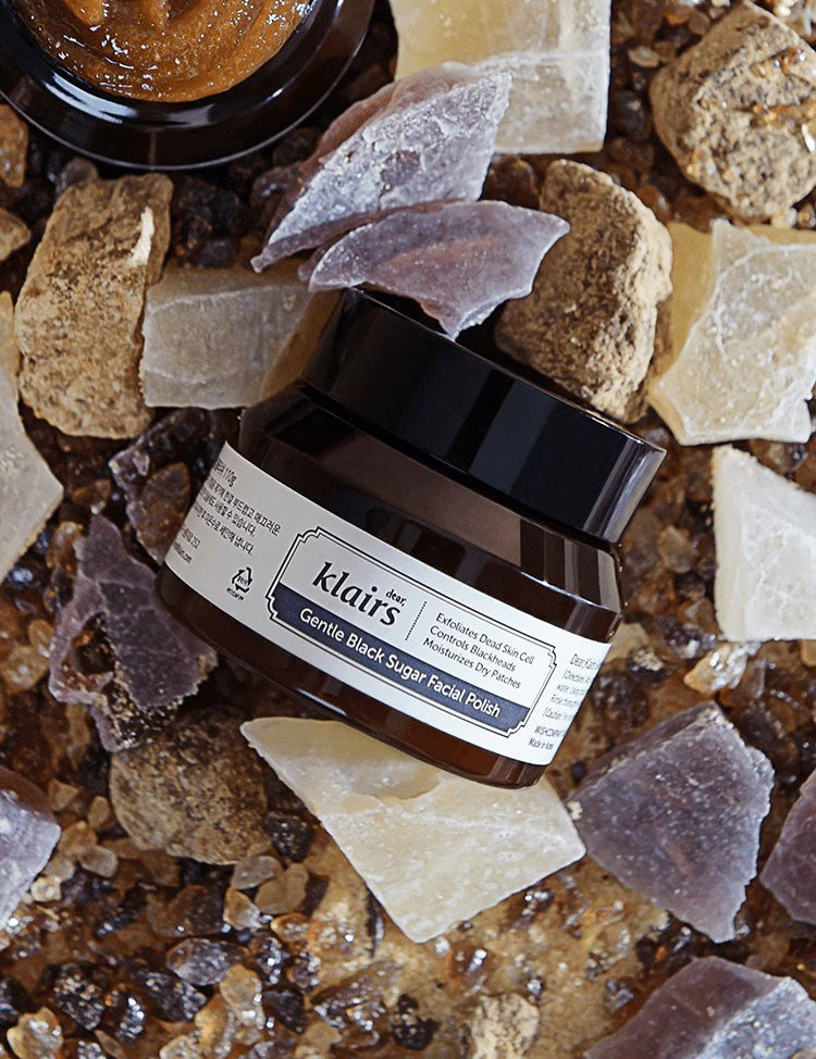 Klairs Gentle Black Sugar Facial Polish in a sleek jar surrounded by natural textured stones and sugar crystals on a rustic surface, highlighting its exfoliating properties.
