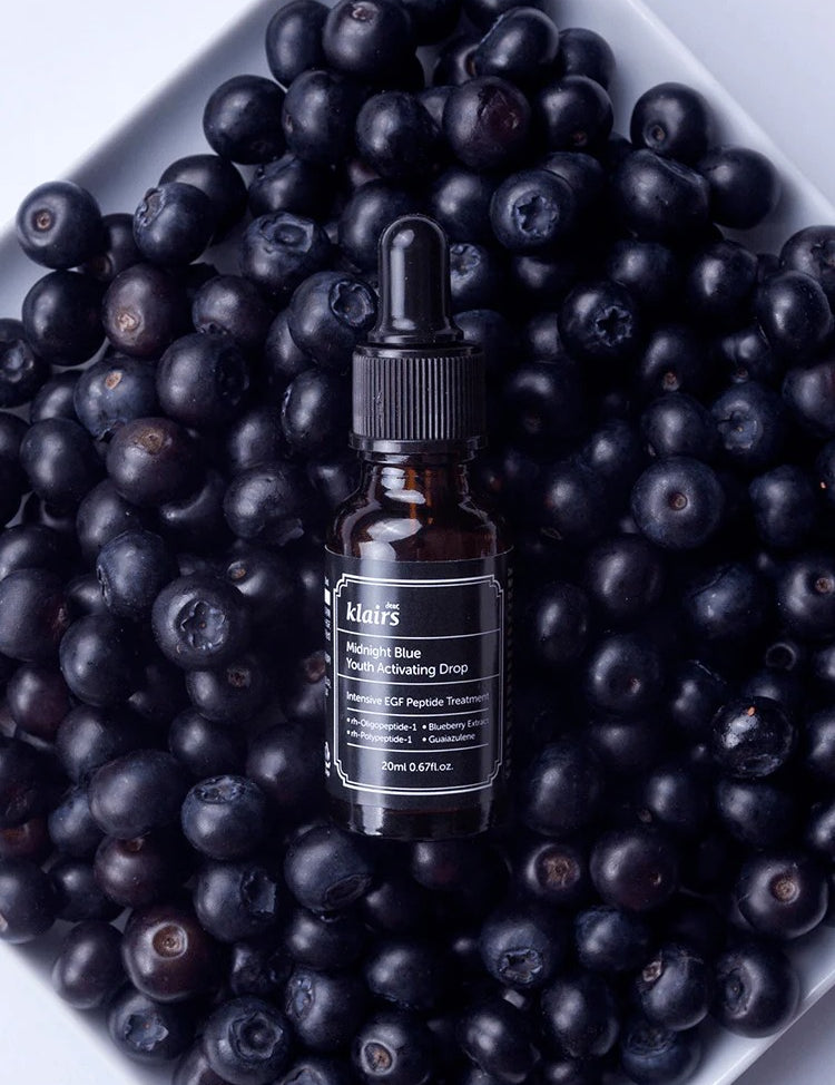 Klairs Midnight Blue Youth Activating Drop bottle placed on a bed of fresh blueberries, highlighting its antioxidant-rich formula and natural ingredients.