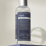 Klairs Supple Preparation Unscented Toner bottle with a sleek design and detailed label, elegantly displayed on a purple pedestal, emphasizing its hydrating and soothing properties.