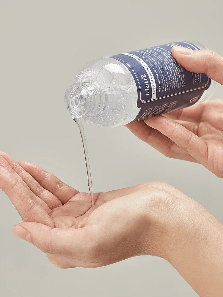 A person pouring Klairs Supple Preparation Unscented Toner into the palm of one hand, highlighting its clear, lightweight texture against a neutral background.