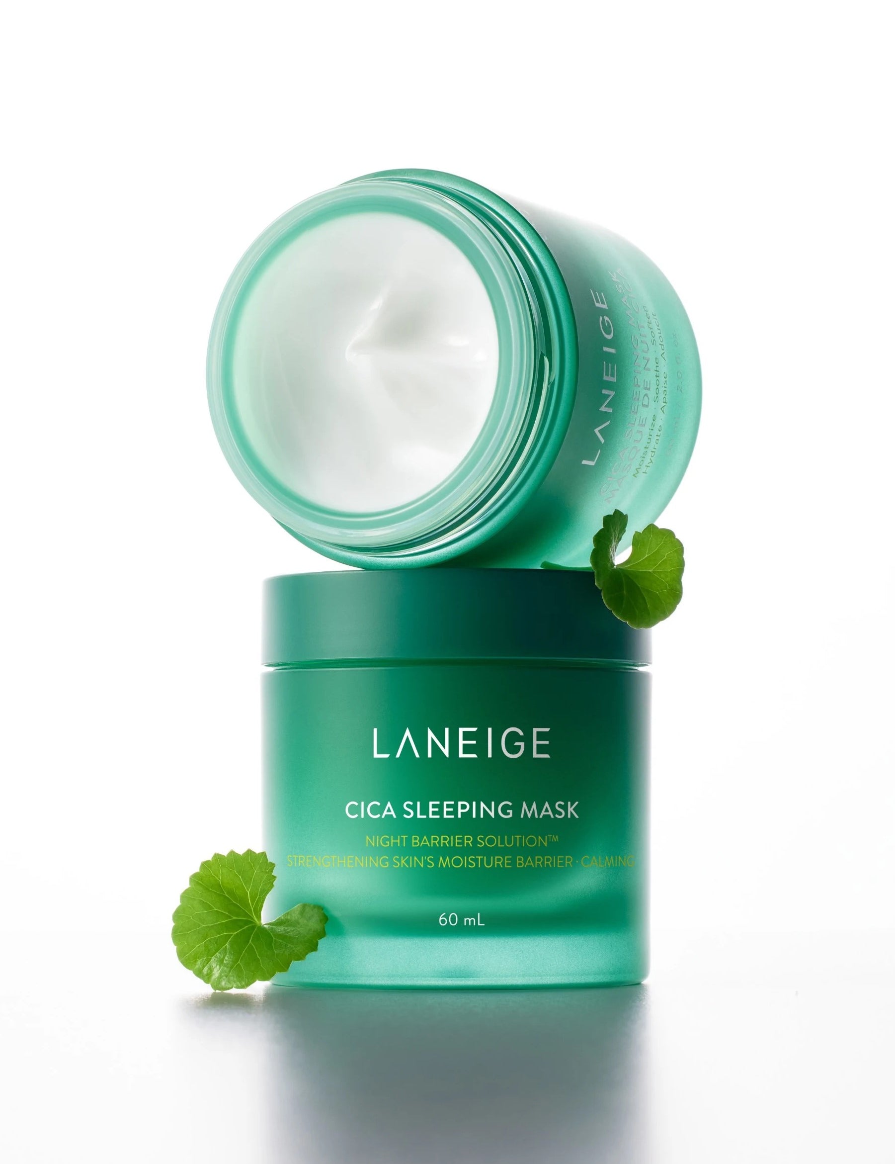 A green jar of Laneige Cica Sleeping Mask opened to reveal creamy texture, with a Centella Asiatica leaf beside it on a white background, highlighting its key ingredient.