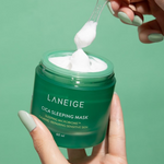 Two hands holding a green jar of Laneige Cica Sleeping Mask, with a plastic spatula scooping creamy white texture against a matching green background.