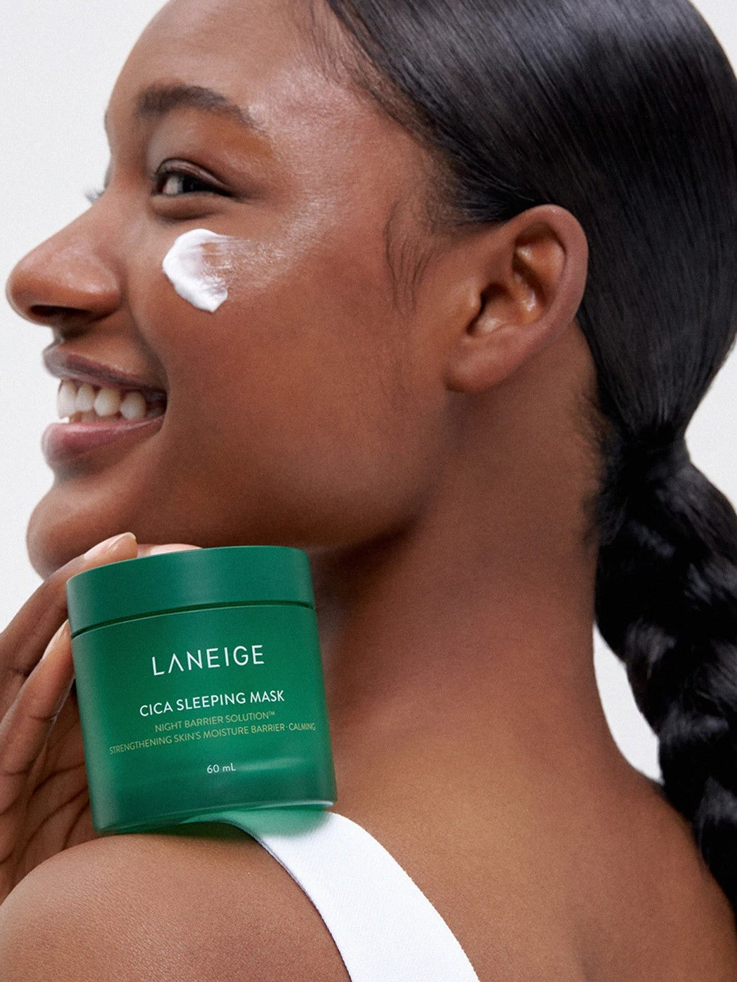 A model with sleek hair holding a green jar of Laneige Cica Sleeping Mask against her shoulder, highlighting skin hydration and barrier support.