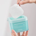 A hand holding a turquoise container of Mediheal Madecassoside Blemish Pad, lifting a cotton pad out with a clear tool, showcasing ease of use.