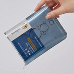 A hand holds the Mediheal N.M.F. Nude Gel Mask package, with essence spilling out to highlight its hydrating benefits.