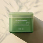 A green jar of Mediheal Teatree Trouble Pad on a light surface, emphasizing its day and night skincare benefits.