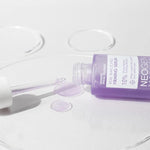 Neogen Bakuchiol Firming Serum bottle with a dropper, spilling vibrant purple liquid onto a white surface, emphasizing its lightweight texture and firming benefits.