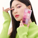 A model in a bright green sweater holds the Romand Better Than Palette Energetic Series in Berry Fuchsia Garden, showcasing the eyeshadow applied on her eyes.