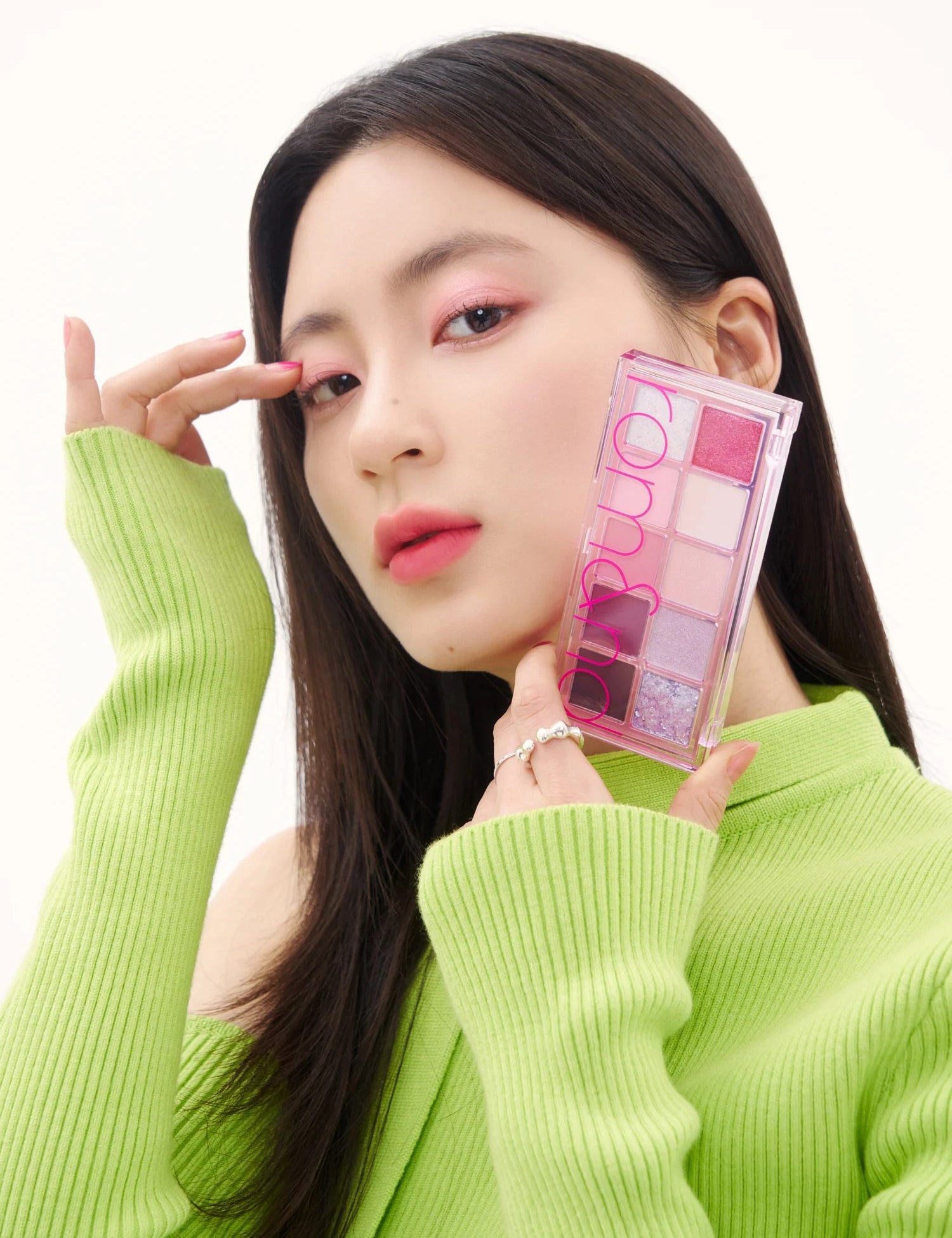 A model in a bright green sweater holds the Romand Better Than Palette Energetic Series in Berry Fuchsia Garden, showcasing the eyeshadow applied on her eyes.