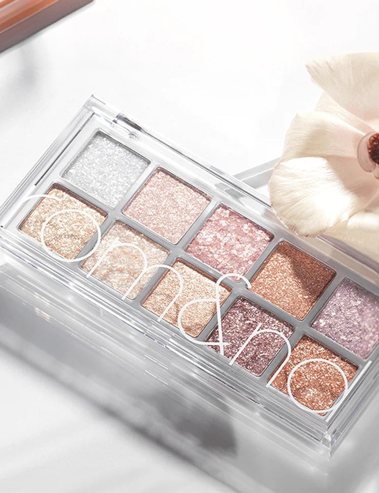 Eyeshadow palette Romand Better Than Palette Light and Glitter Garden, featuring ten shimmering shades from silver to pink and rose gold, styled with a delicate flower.
