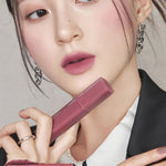 A model wearing Romand Blur Fudge Tint in the shade Mauvish, showcasing the soft matte texture on her lips.