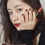 A model wearing Romand Blur Fudge Tint in the shade Radwood, showcasing the soft matte texture on her lips.