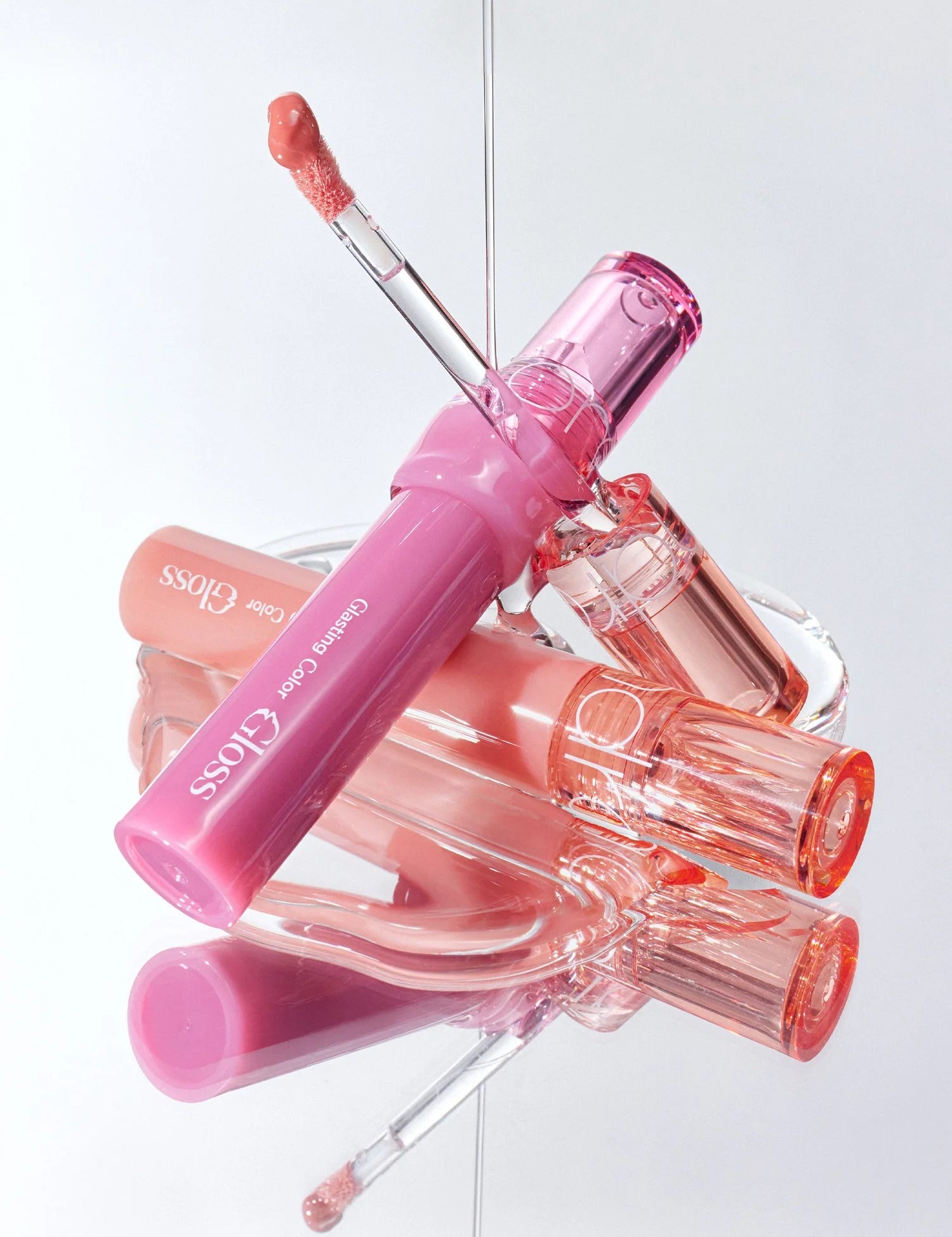 A collection of Romand Glasting Color Gloss tubes displayed elegantly, featuring a pink-tinted flexible applicator and light-reflecting shine.