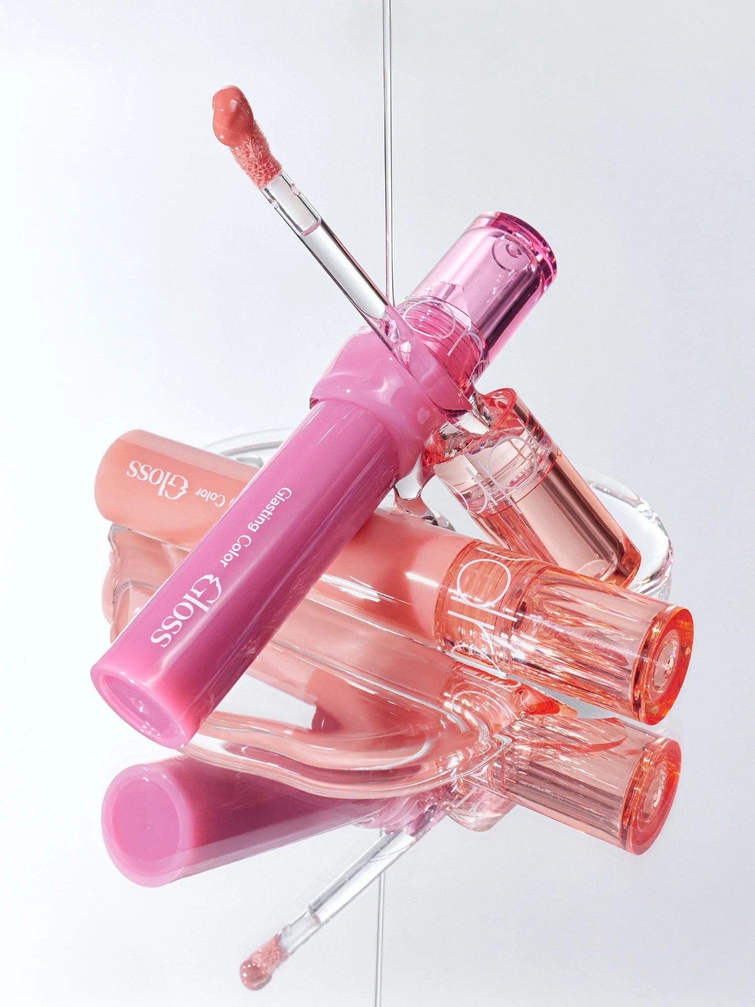 A collection of Romand Glasting Color Gloss tubes displayed elegantly, featuring a pink-tinted flexible applicator and light-reflecting shine.