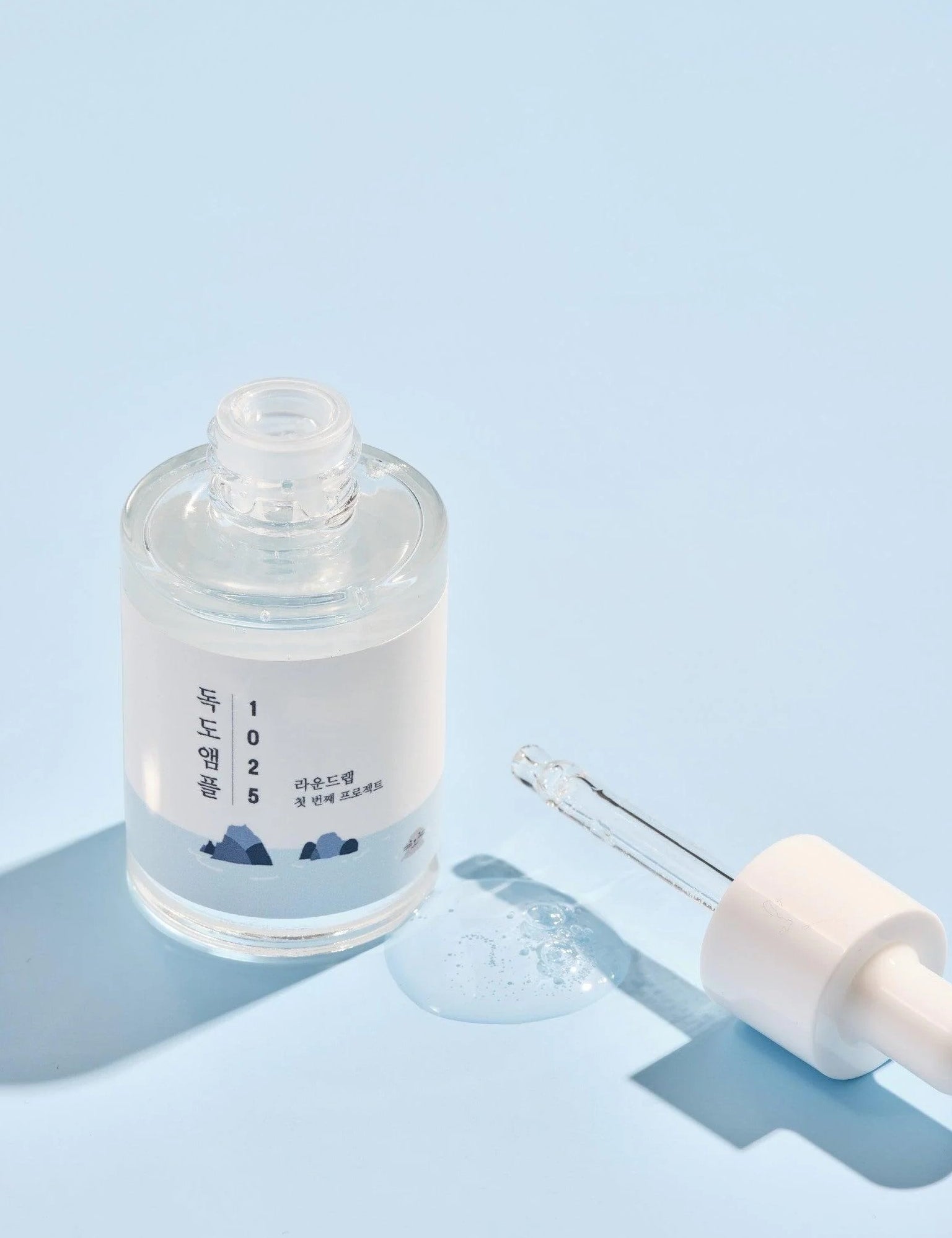Round Lab 1025 Dokdo Ampoule with dropper and droplet, set against a light blue background.
