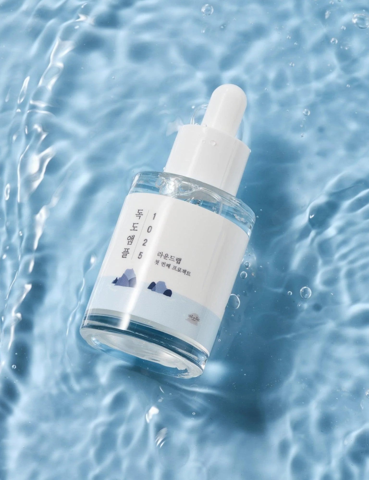 Round Lab 1025 Dokdo Ampoule resting on water, featuring a minimalist mountain-themed design.