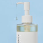 Round Lab 1025 Dokdo Cleansing Oil with liquid dripping from the nozzle, set against a soft blue background.